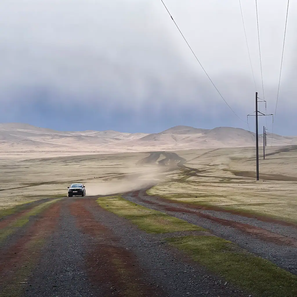 A car on a long dirt road across the steppe
