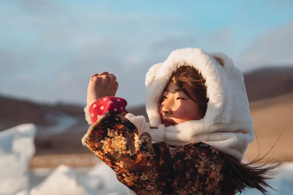 A child in a fur-trimmed winter coat, laughing in the snow