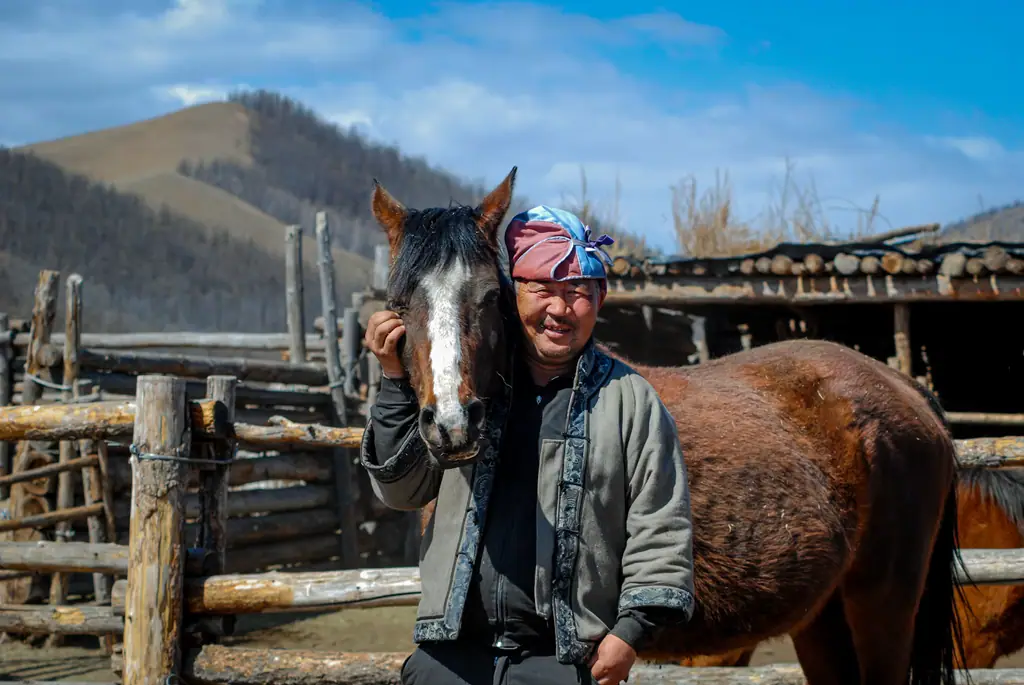 A herder laughing beside his horse at a winter camp